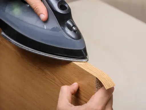 Persona aplica cinta de cantear a un borde de madera con una plancha.
