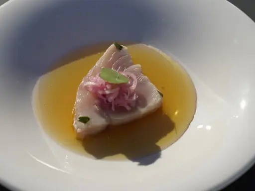 Bonito fresco en un caldo dorado, coronado con cebolla morada y una hoja verde. Un plato ligero y sabroso.