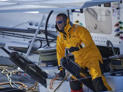 Skipper en tenue jaune, concentré, manœuvre un winch sur un bateau Banque Populaire.