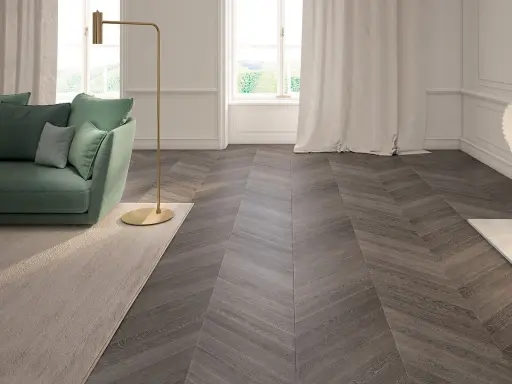 Elegante soggiorno con divano verde, lampada dorata e un tappeto beige. Il pavimento in parquet a spina di pesce, con un colore scuro e venature evidenti, completa l'arredamento.