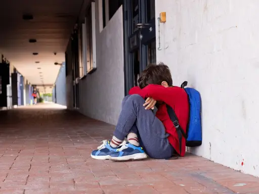 Ein Junge sitzt traurig in einem Schulflur, den Kopf in den Armen vergraben. Er fühlt sich allein, als ob mein Kind gemobbt wird und der Lehrer nichts tut.