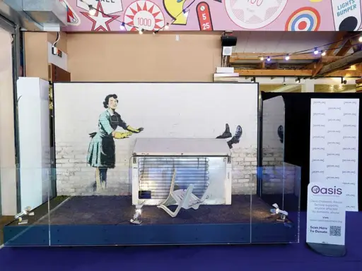 Banksy's "Girl with Balloon" installation, a prime example of art investment, displayed with a fridge and chair.