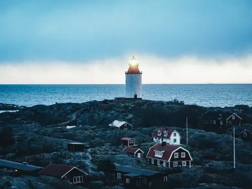 En fyr lyser över klippor och röda hus vid havet. En idyllisk plats för unika hotell Sverige.