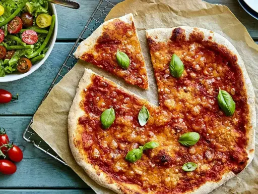 En härlig hemmagjord pizza med tomatsås och ost, toppad med färsk basilika. Bredvid en fräsch sallad med gröna bönor och körsbärstomater.