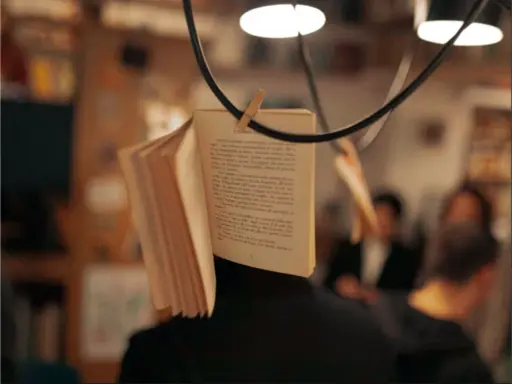 Un libro aperto, appeso per creare una scena da foto libri aesthetic. Le pagine sono piene di testo, con persone sfocate sullo sfondo.