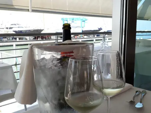 Un bicchiere di vino bianco e una bottiglia in un secchiello di ghiaccio, con vista sul porto e yacht, al ristorante club nautico Rimini.