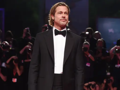 Brad Pitt looking dapper in a classic tuxedo with a black cummerbund and bow tie, posing for photographers.