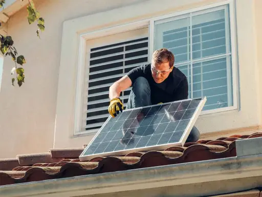 Instalación de placas solares en comunidad de vecinos. Un hombre con guantes y gafas de seguridad coloca un panel solar en un tejado.