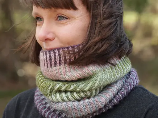 Woman wearing a colorful knitted cowl in shades of green, pink, and purple.