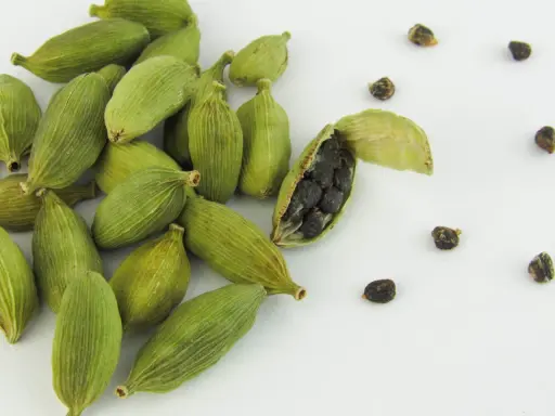 Gousses de cardamome verte, dont une ouverte révélant ses graines noires. Découvrez les cardamome bienfaits pour la santé et la cuisine.
