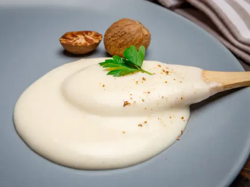 Krämig bechamelsås på en tallrik med muskotnötter och persilja. Perfekt för ditt bechamelsås recept.