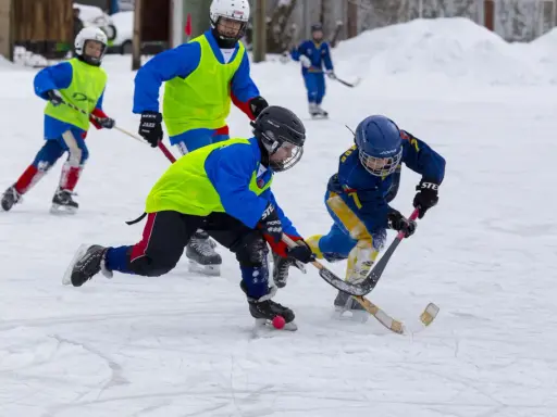 Barn i full fart med hockeyklubbor och hjälmar, ivriga att vinna pucken. De har roligt med lekar på isen.