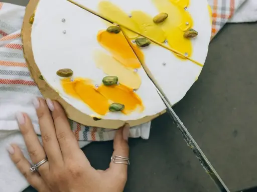 Delikatny tort z pistacjami i żółtym kremem, pokazany w momencie, jak kroić tort.
