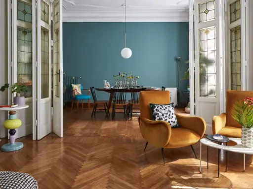 Un soggiorno che unisce con successo arredamento classico e moderno: sedie in velluto ocra, tavolino di design e porte antiche con vetri colorati.