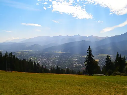 Widok z Gubałówki na Butorowy Wierch i Tatry. Słoneczny dzień, chmury na niebie.