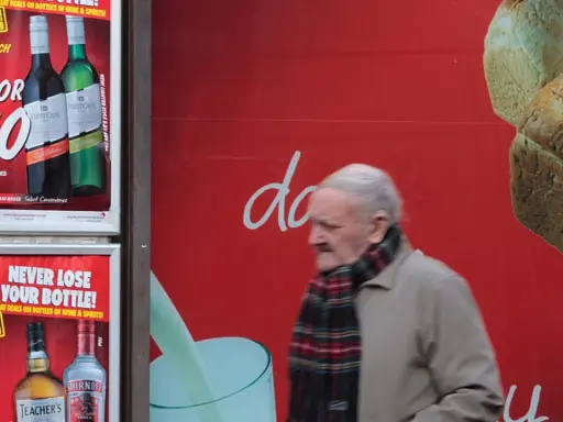 Starszy mężczyzna mija reklamę z promocją na alkohol. Włochy ceny alkoholu są atrakcyjne.