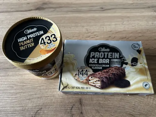 Gdzie kupić lody proteinowe? Na zdjęciu widać opakowania lodów Gelatelli: kubełek masło orzechowe i batoniki ciasteczkowe.