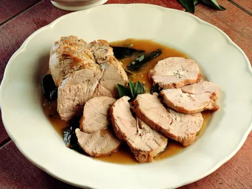 Delizioso arrosto di tacchino affettato, servito con salsa e foglie di salvia su un piatto bianco.