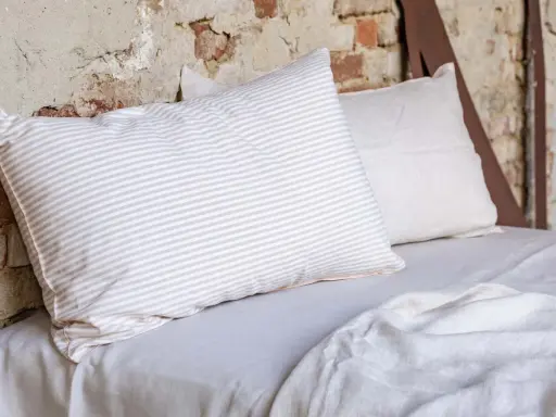 Cuscini a righe e tinta unita su un letto coperto da lenzuola di lino. Le caratteristiche del linone tessuto sono evidenti nella texture naturale.