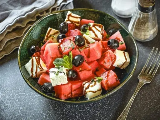 Erfrischender Melonen Feta Salat mit schwarzen Oliven und Minze, beträufelt mit Balsamico-Dressing. Perfekt für heiße Tage!