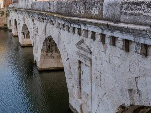 Il Ponte di Tiberio a Rimini, con i suoi archi in pietra bianca che si specchiano sull'acqua scura, testimonia secoli di storia.