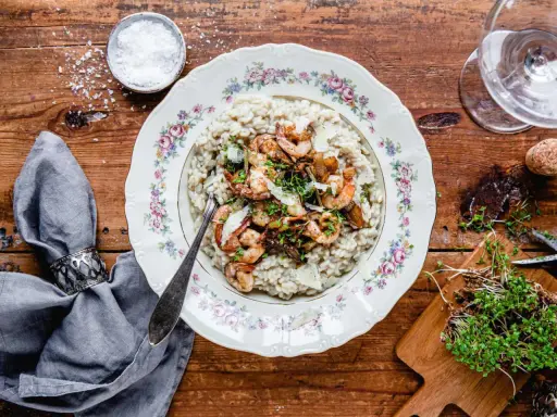 En tallrik med lyxig risotto toppad med räkor och svamp, serverad på ett vackert mönstrat fat.