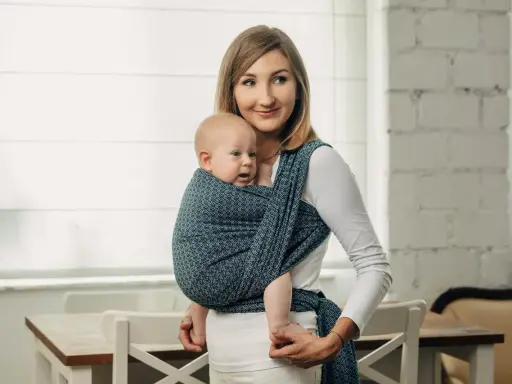 Uśmiechnięta mama nosi dziecko w chuście tkanej, która zapewnia komfort i bezpieczeństwo.