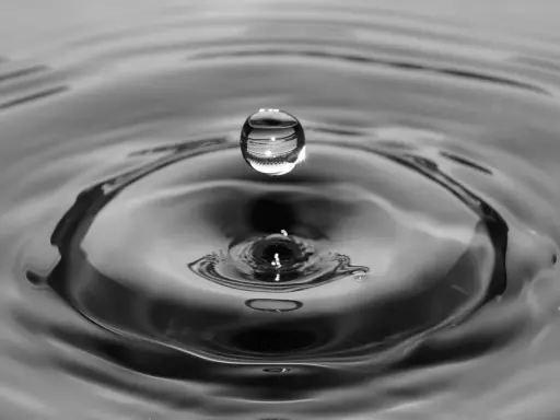 Goutte d'eau en suspension au-dessus de son impact, créant des ondulations. L'eau calcaire reflète la lumière.