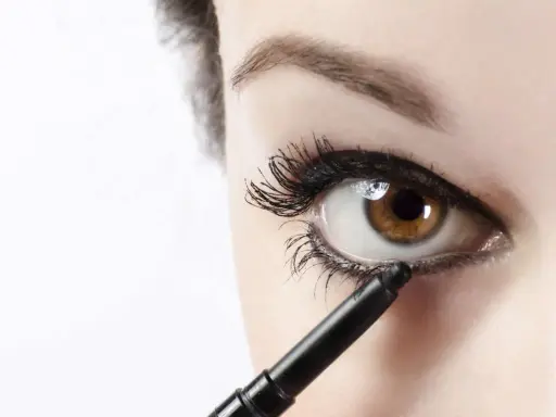 Ojo marrón recibiendo el toque final de maquillaje ojos negro con un lápiz.