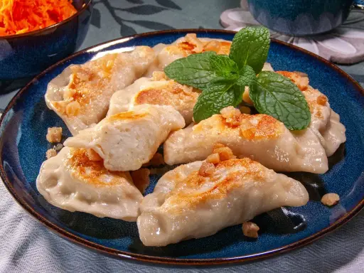 Pyszne pierogi ruskie przepis na talerzu, posypane skwarkami i udekorowane miętą.