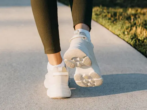 Füße in weißen Sneakern und grünen Leggings gehen auf einem Gehweg. Ein Hauch von japanischem Gehen in der Abendsonne.