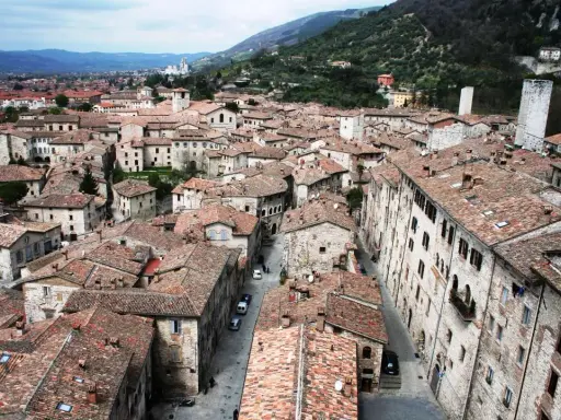 Panoramica di tetti rossi e antichi edifici in pietra, con torri medievali che svettano. Un paesaggio che ricorda l'Umbria, tra Assisi e Gubbio.