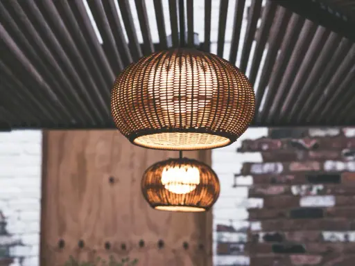 Dos lámparas de mimbre esféricas cuelgan bajo un techo de listones. La luz cálida que emiten crea un ambiente acogedor, con unos lumenes por m2 perfectos para relajarse.