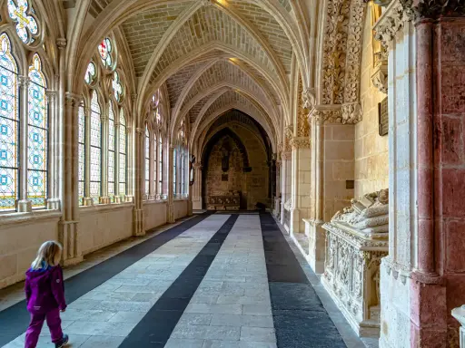 Ein Kind erkundet die gotischen Gänge der Burgos Kathedrale, vorbei an bunten Glasfenstern und kunstvollen Sarkophagen.