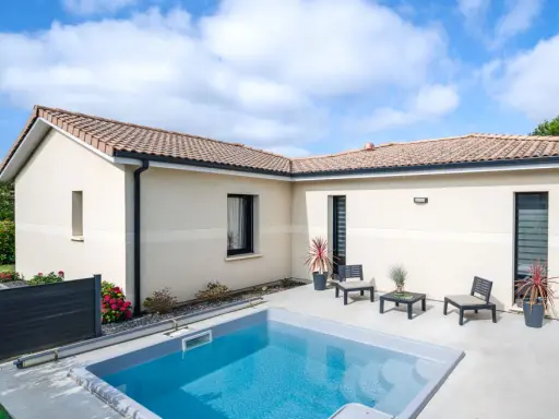 Vue aérienne d'une maison moderne avec piscine, le **plan maison en L** est bien visible, entouré de verdure.