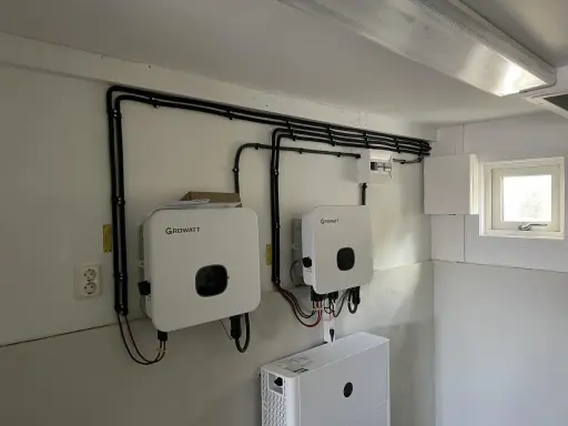 Två Growatt-växelriktare och en batteribank för solceller monterade på en vägg. Kablar dras snyggt längs väggen.