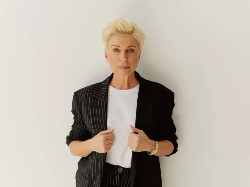 Elegancka kobieta z blond włosami, w czarnej marynarce w paski, pokazuje, jak powinna leżeć marynarka, podkreślając jej stylowy krój.