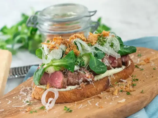 En saftig steak sandwich med möra skivor av biff, krämig majonnäs, färska gröna blad, krispig lök och riven parmesanost på rostat bröd.