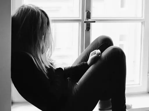 Una joven sentada en la ventana, con la mirada perdida. Un momento para reflexionar sobre qué decirle a tu hija cuando le rompen el corazón.