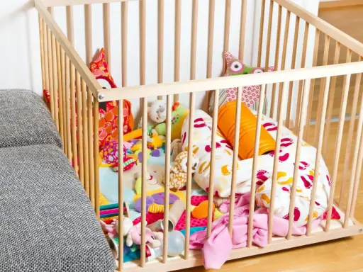 Ein bunter Spielteppich mit vielen Kuscheltieren und Kissen in einem Laufstall. Ja oder nein, diese sichere Spielzone für Babys?
