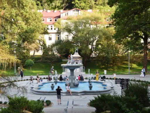 Rymanów Zdrój atrakcje: ludzie odpoczywają przy fontannie w parku zdrojowym, w tle budynek uzdrowiskowy.