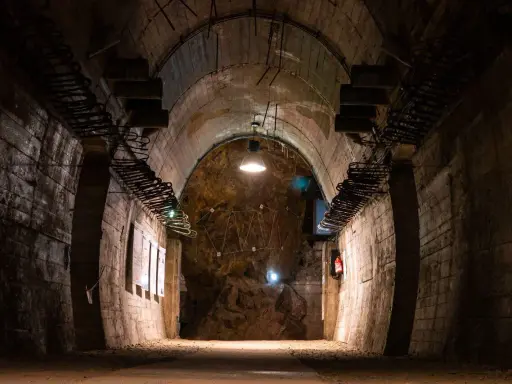 Wnętrze tunelu w Górach Sowich. Betonowe ściany, łukowe sklepienie i skalna grota z instalacją świetlną.