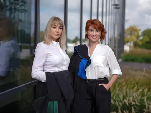Dwie prawniczki w togach przed nowoczesnym budynkiem.