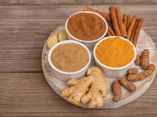 Poudre de curcuma, gingembre frais et bâtons de cannelle sur une planche en bois. Idéal pour un thé réconfortant au curcuma et miel.