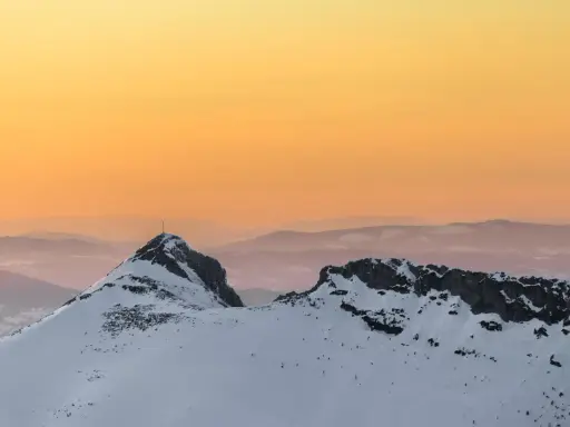 Giewont zimą o zachodzie słońca. Ośnieżone szczyty Tatr w odcieniach pomarańczy i różu.