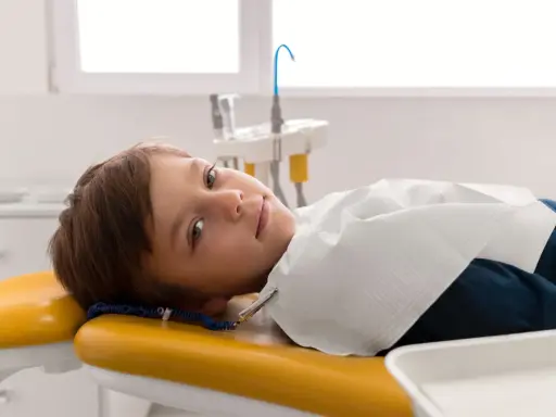 Chłopiec leży na żółtym fotelu dentystycznym, przygotowany do leczenia zębów pod narkozą.