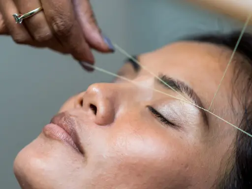 Une main utilise un fil pour épiler ses sourcils.