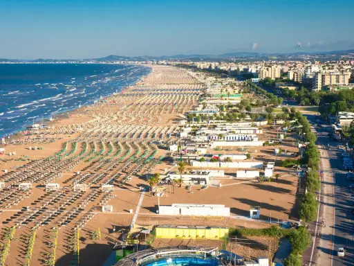 La riviera romagnola dove andare: una distesa infinita di ombrelloni e lettini sulla sabbia dorata, con il mare azzurro e la città sullo sfondo.