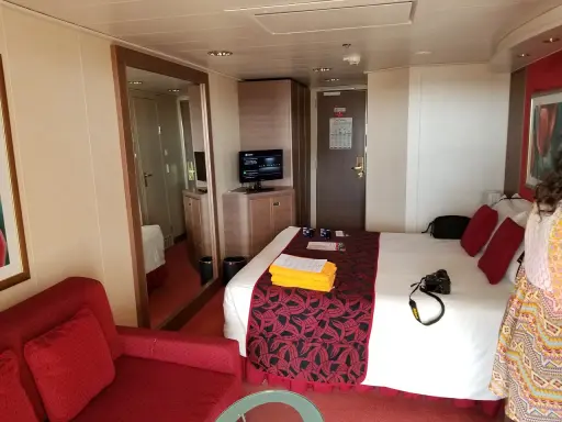 Cabina MSC Musica con letto, divano rosso, specchio e TV. Perfetta per una vacanza in crociera.