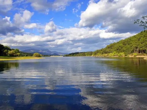 El embalse La Jarosa, con su agua serena reflejando el cielo nublado y rodeado de verdes colinas, invita a la calma.